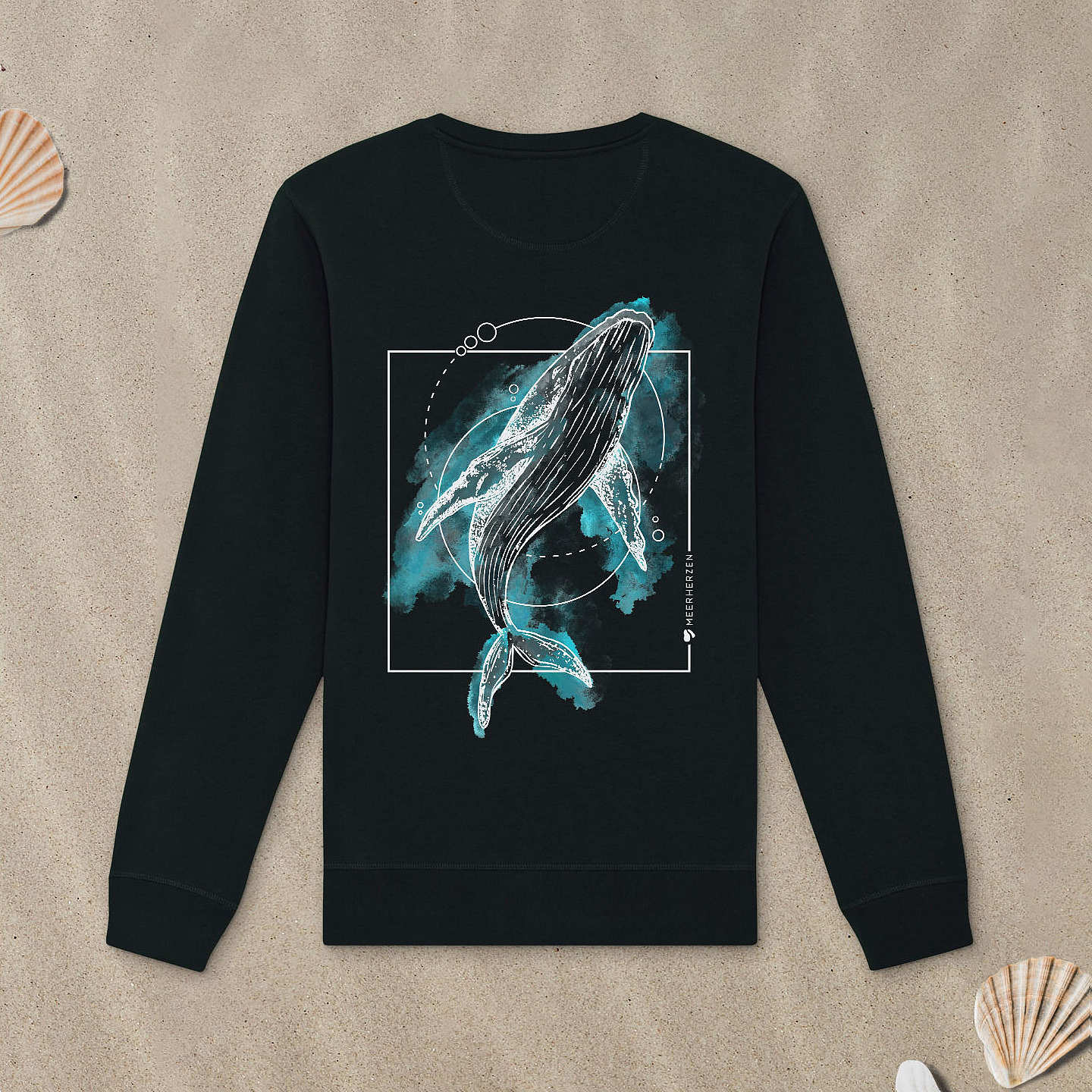 Schwarzes Sweatshirt mit Buckelwal-Motiv mit Aquarell-Farben liegt im Sand.