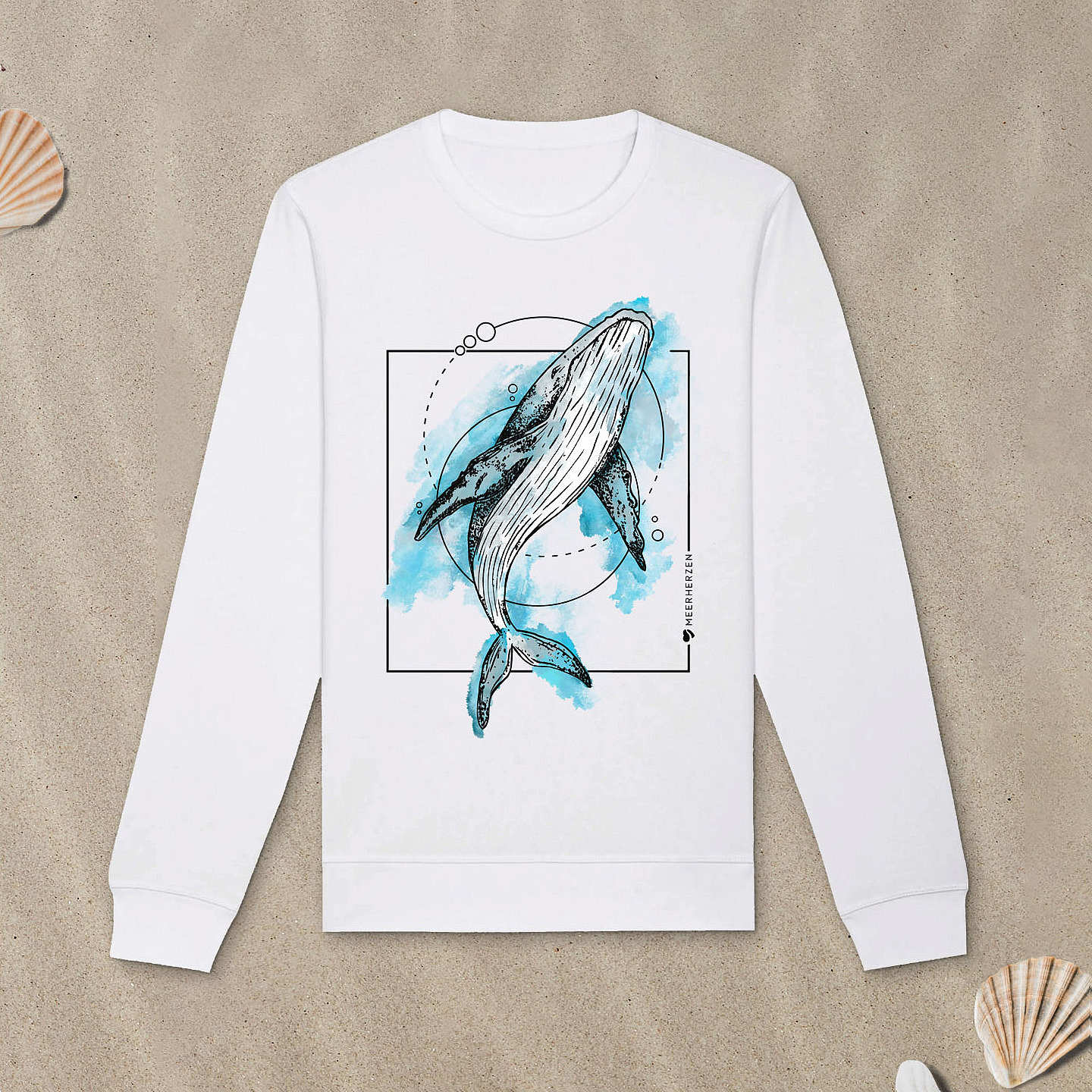 Weißes Sweatshirt mit Buckelwal-Motiv mit Aquarell-Farben liegt im Sand.