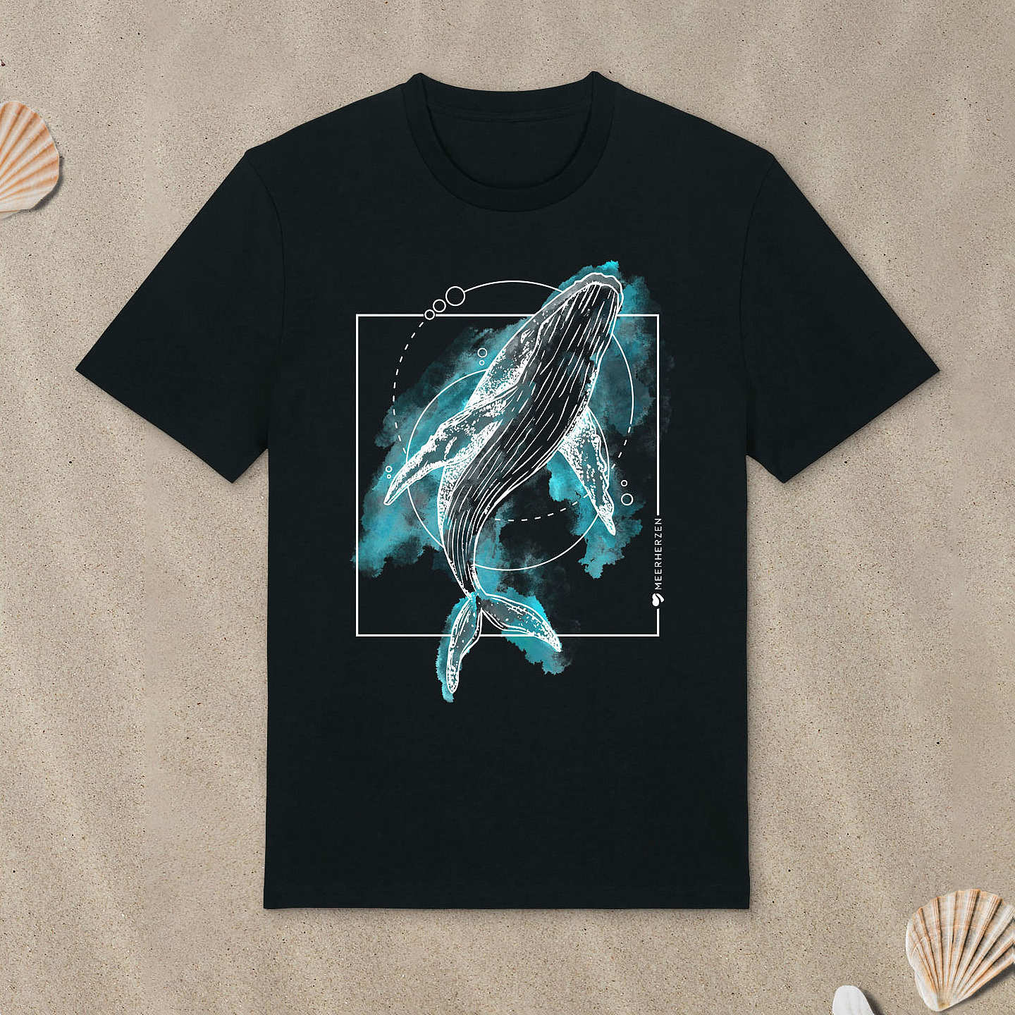 Schwarzes T-Shirt mit Buckelwal-Motiv mit Aquarell-Farben liegt im Sand.