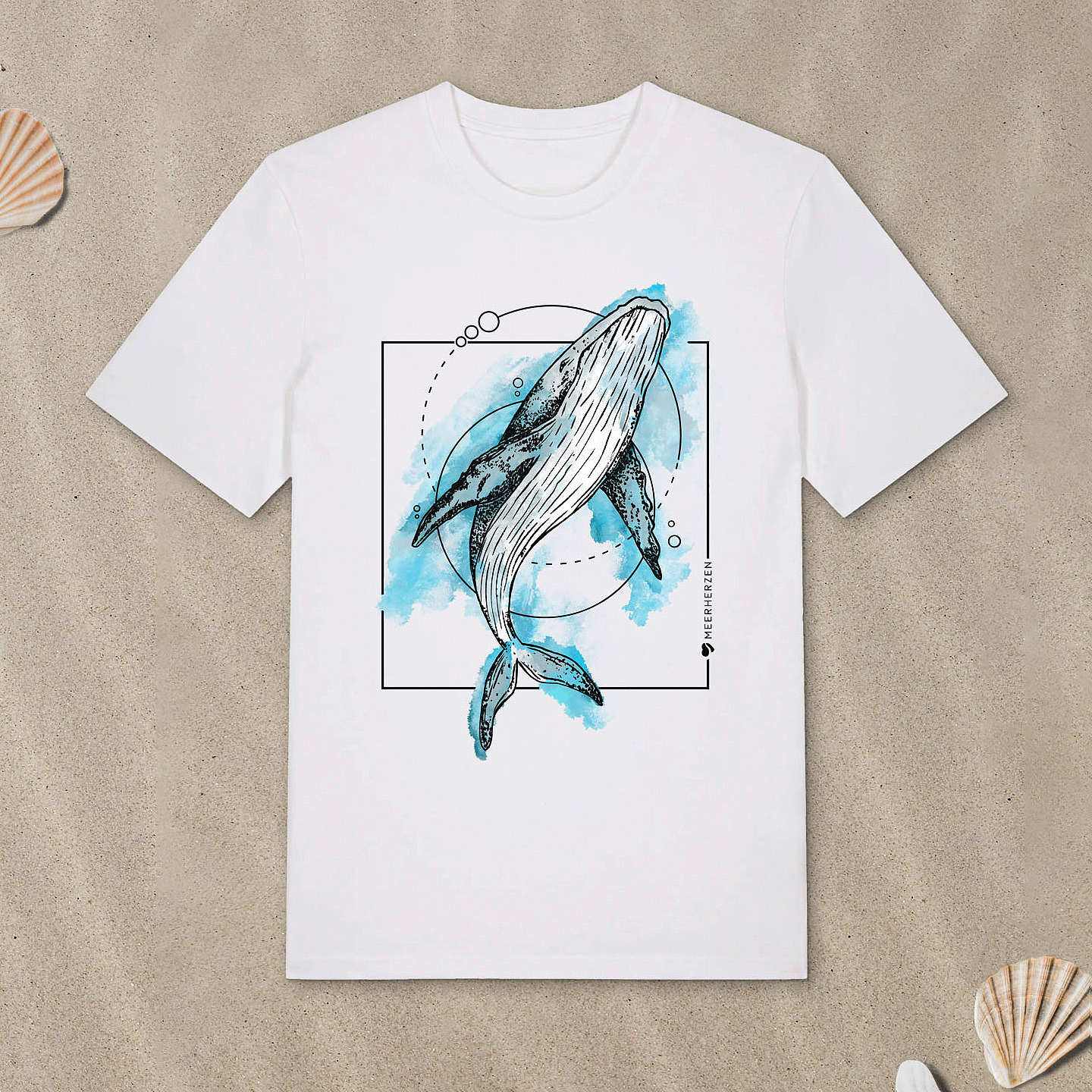 Weißes T-Shirt mit Buckelwal-Motiv mit Aquarell-Farben liegt im Sand.
