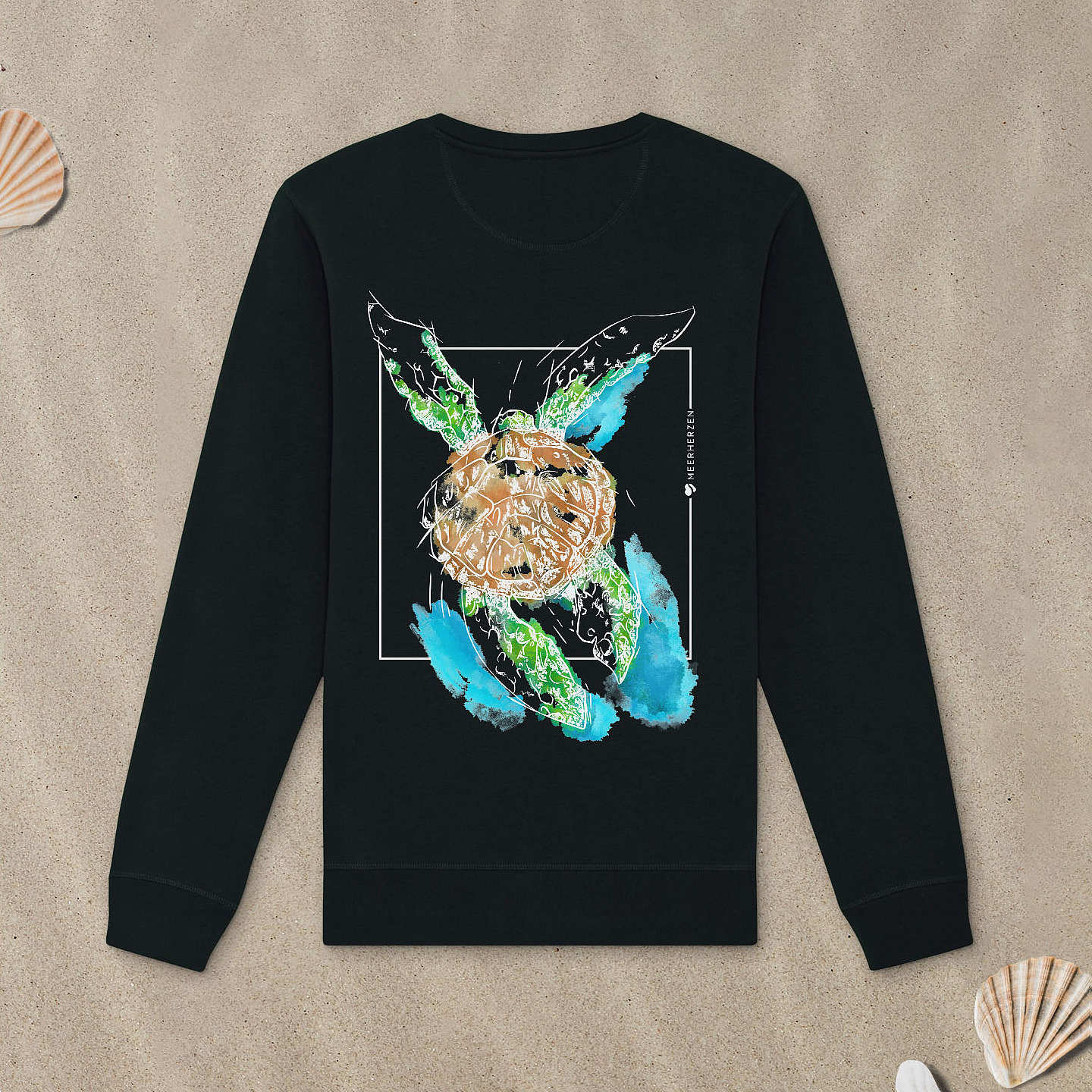 Schwarzes Sweatshirt mit Meeresschildkröte-Motiv mit Astrologie-Elementen liegt im Sand.