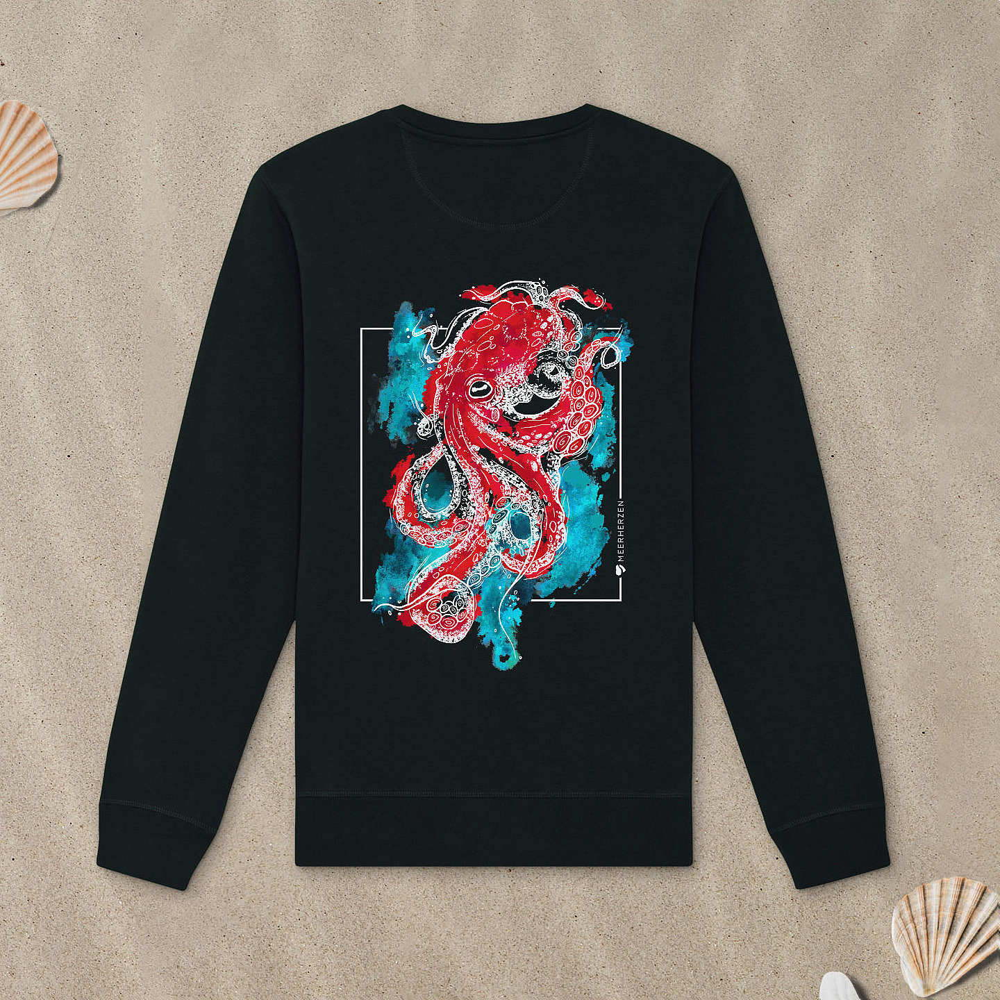 Schwarzes Sweatshirt mit Tintenfisch-Motiv mit bunten Aquarell-Farben liegt im Sand.