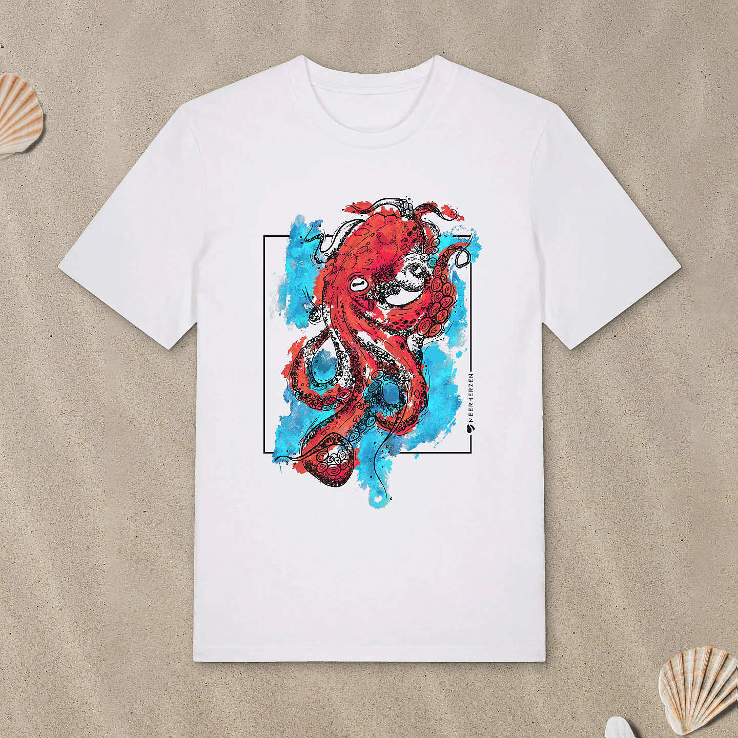 Weißes T-Shirt mit Tintenfisch-Motiv mit bunten Aquarell-Farben liegt im Sand.