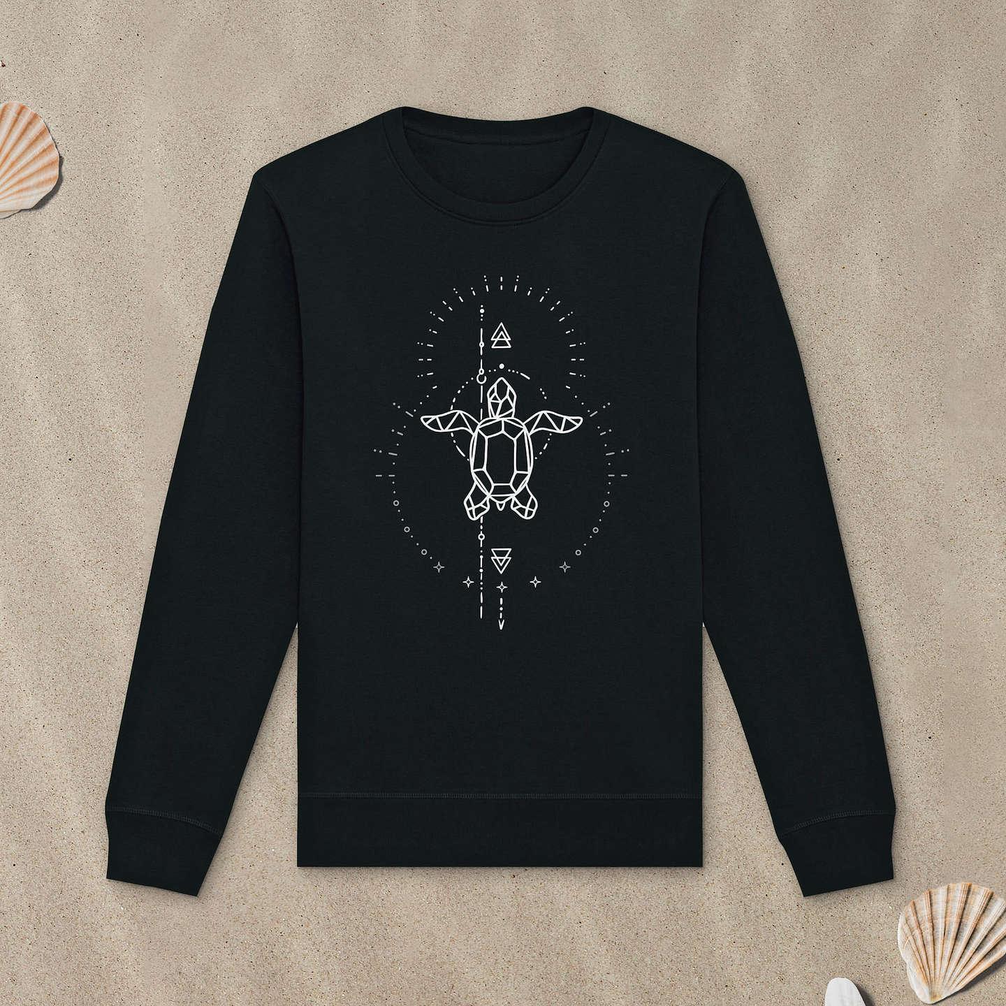 Schwarzes Sweatshirt mit Meeresschildkröte-Motiv mit Astrologie-Elementen liegt im Sand.