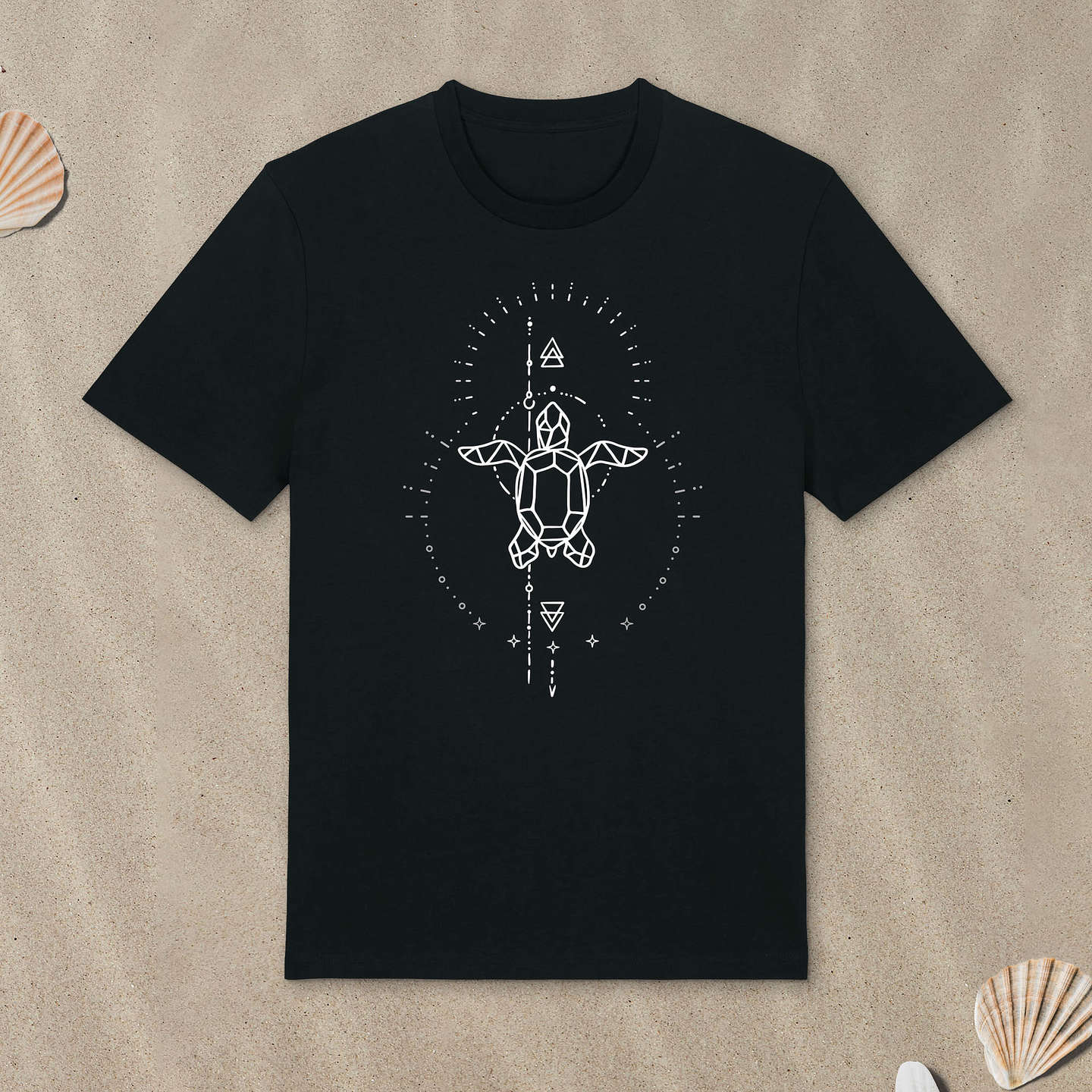 Schwarzes T-Shirt mit Meeresschildkröte-Motiv mit Astrologie-Elementen liegt im Sand.