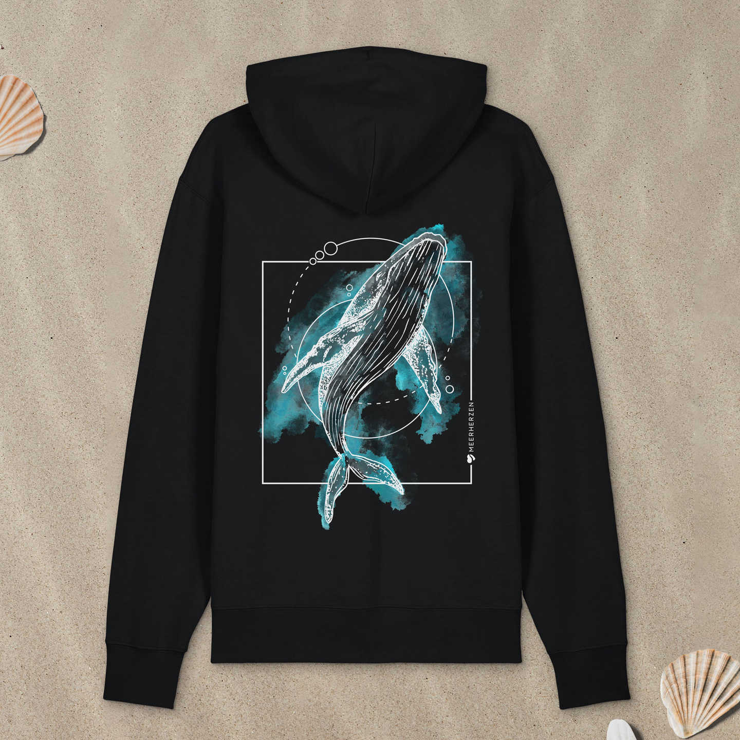 Schwarzer Hoodie mit Buckelwal-Motiv mit bunten Aquarell-Farben liegt im Sand.
