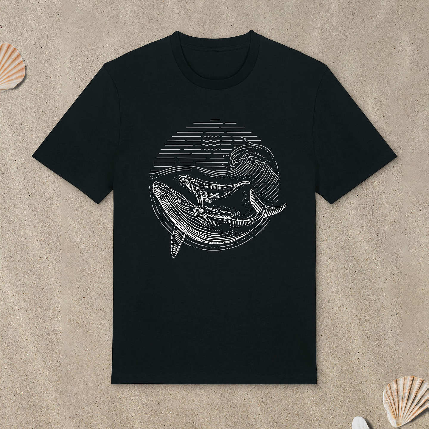 Schwarzes T-Shirt mit Buckelwal-Motiv im Lineart-Stil liegt im Sand.