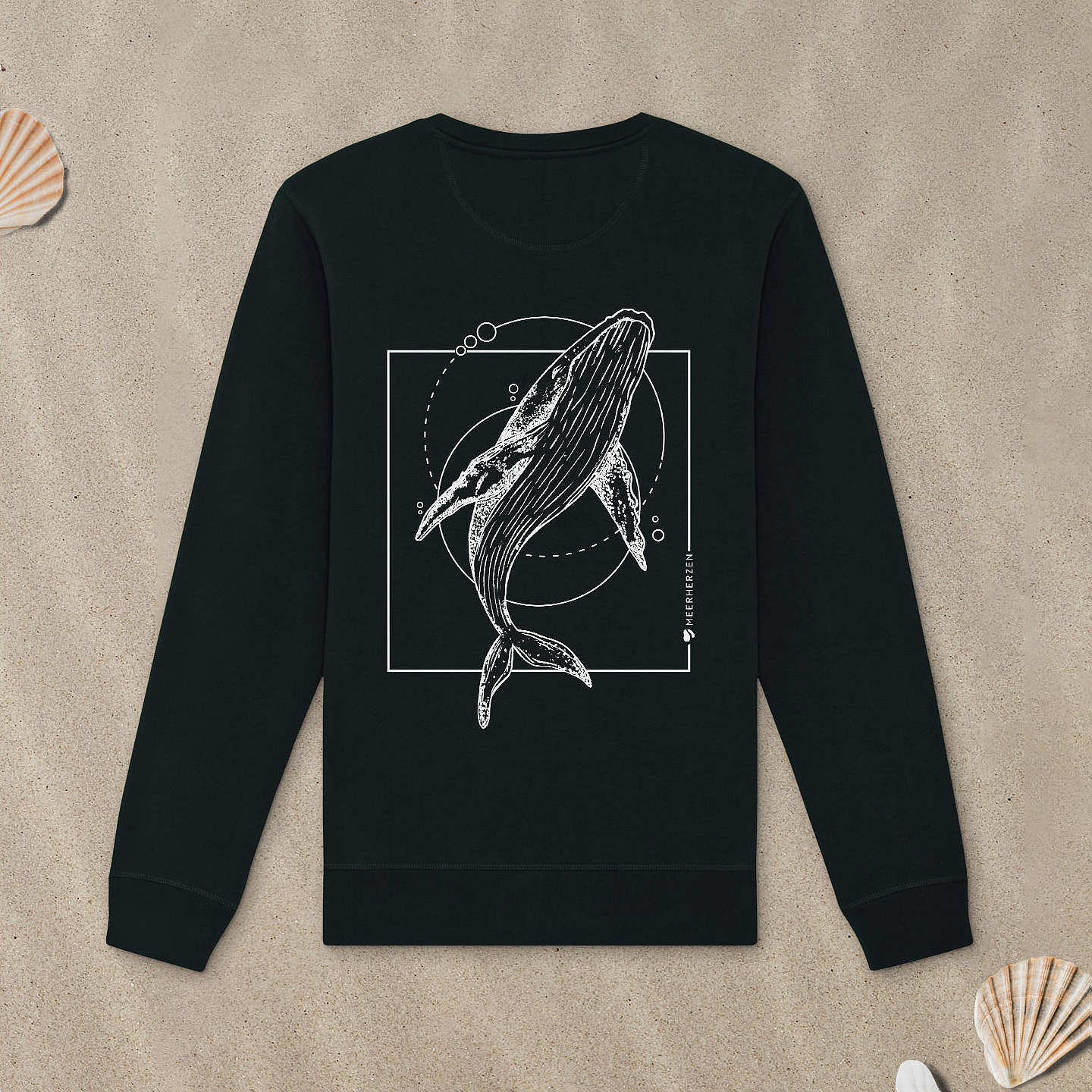 Schwarzes Sweatshirt mit Buckelwal-Motiv liegt im Sand.
