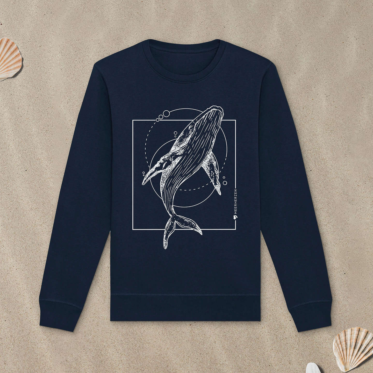Marineblaues Sweatshirt mit Buckelwal-Motiv liegt im Sand.