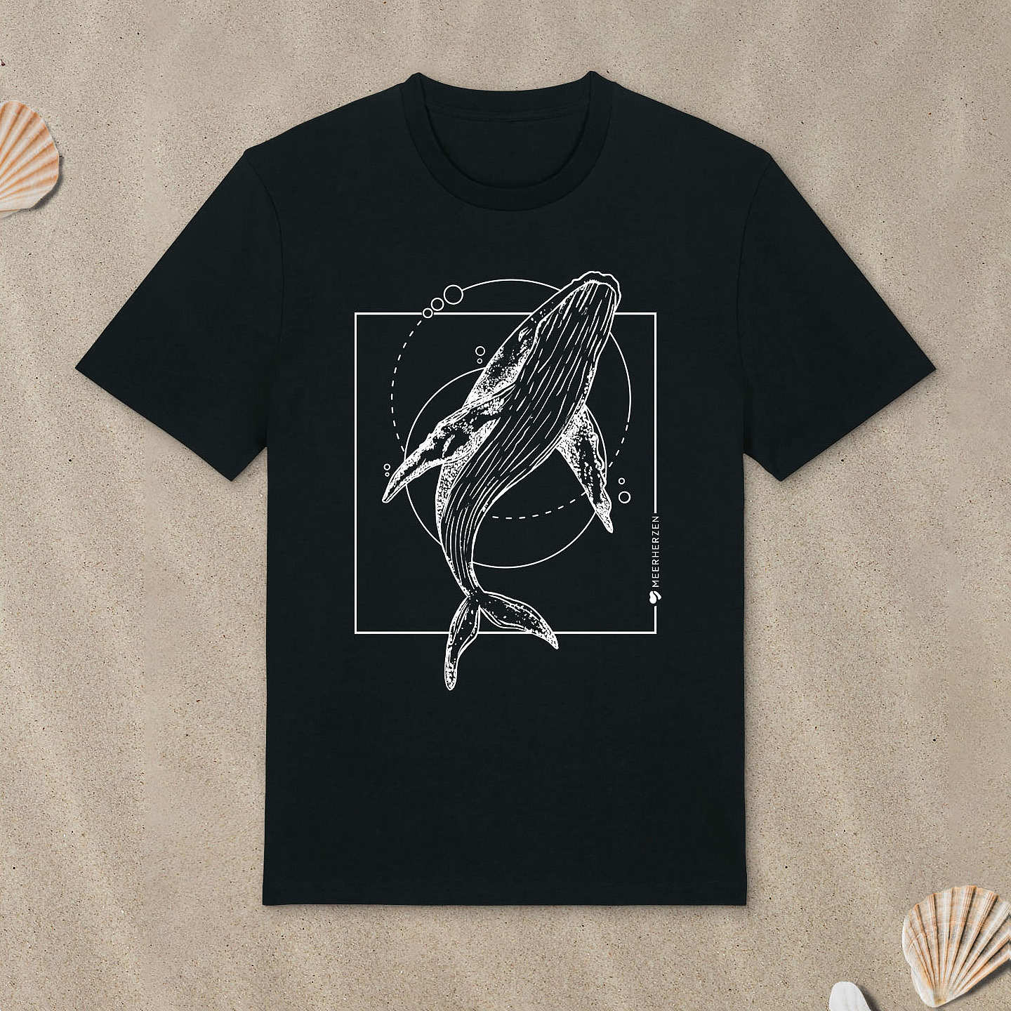 Schwarzes T-Shirt mit Buckelwal-Motiv liegt im Sand.