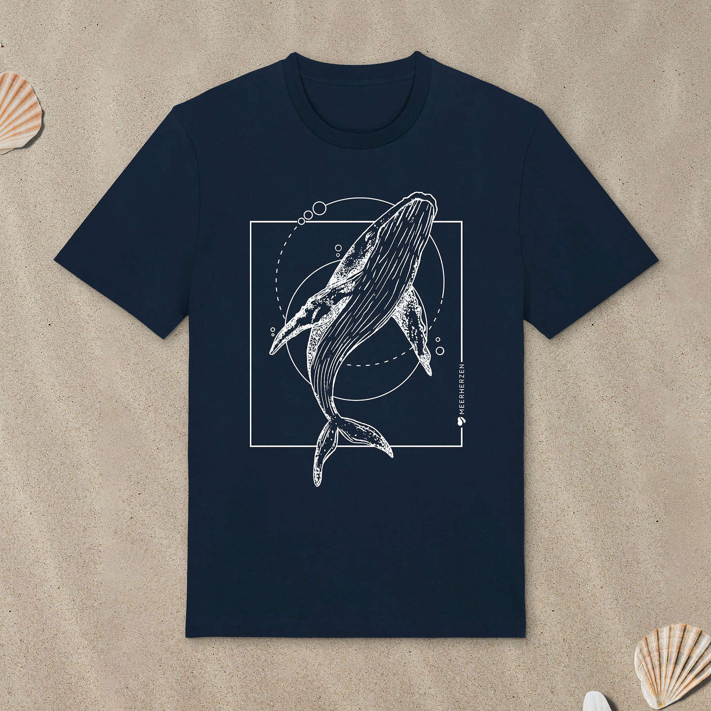 Marineblaues T-Shirt mit Buckelwal-Motiv liegt im Sand.