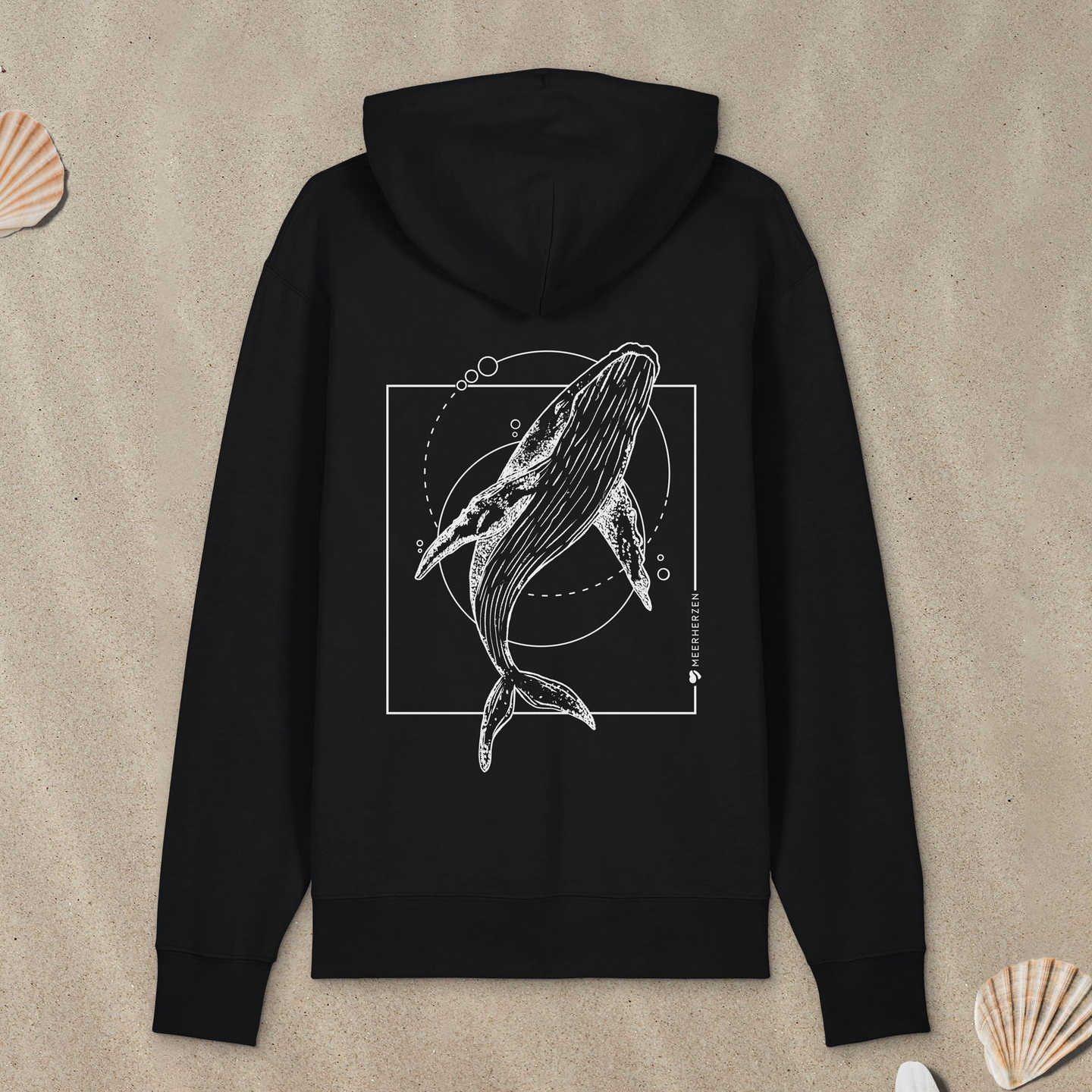 Schwarzer Hoodie mit Buckelwal-Motiv liegt im Sand.