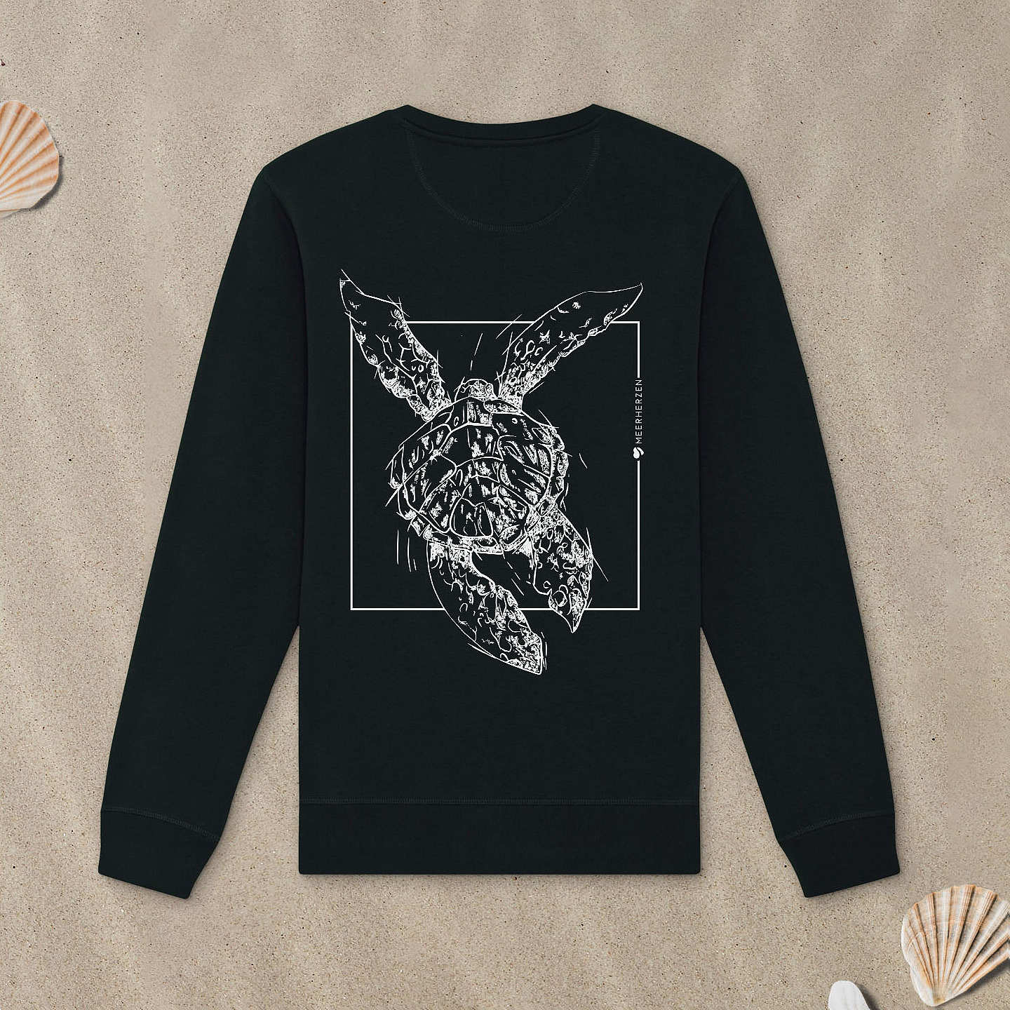 Schwarzes Sweatshirt mit Meeresschildkröte-Motiv mit Astrologie-Elementen liegt im Sand.