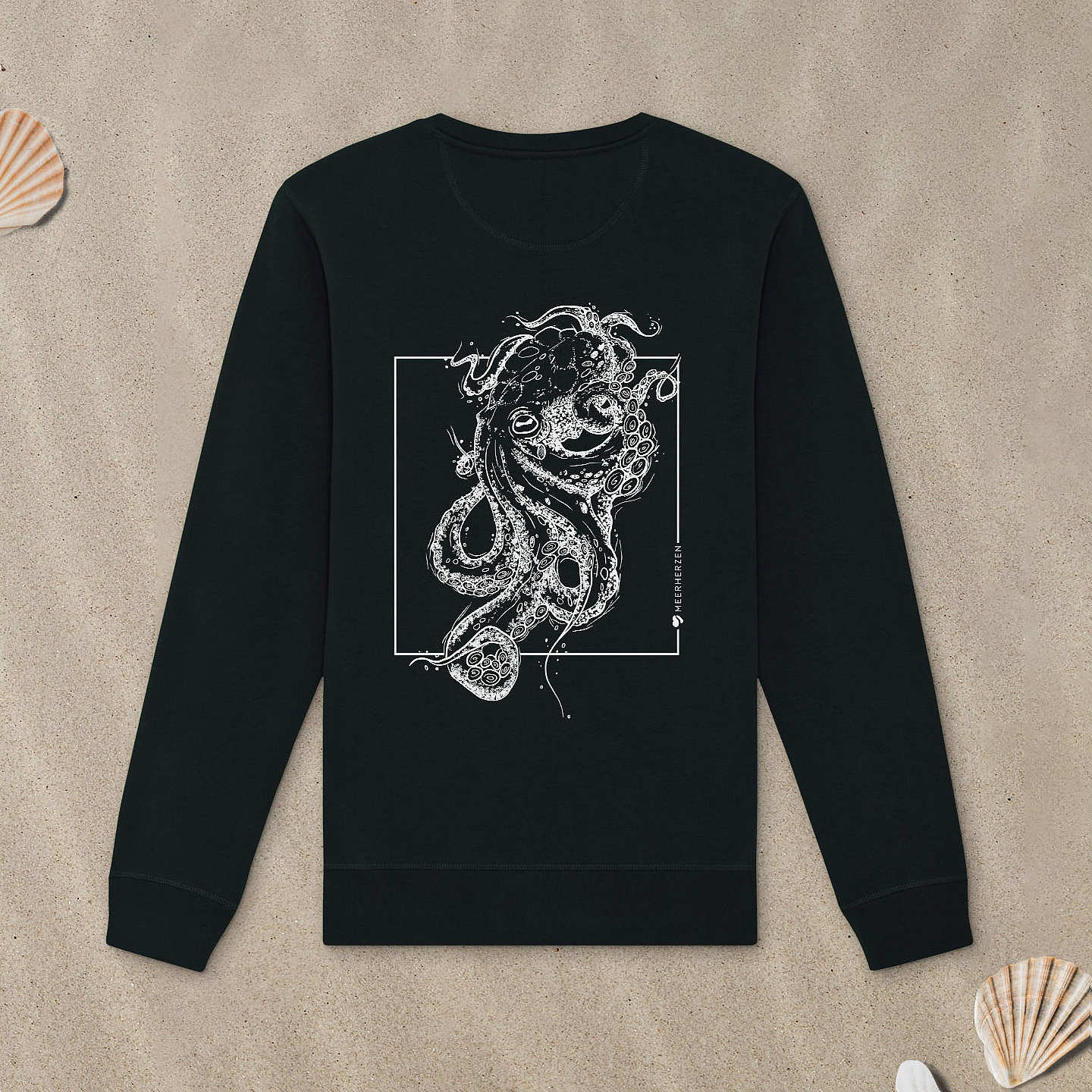 Schwarzes Sweatshirt mit Tintenfisch-Motiv liegt im Sand.