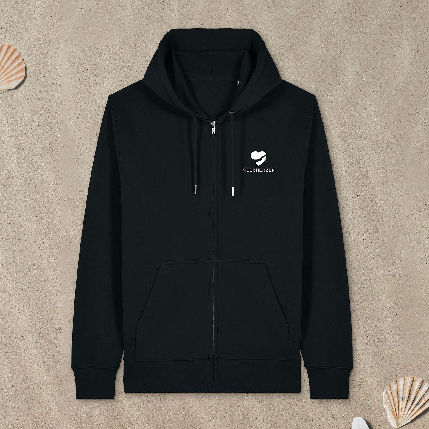 Schwarzer Zipper Hoodie mit Herz-Logo auf der Brust liegt im Sand.